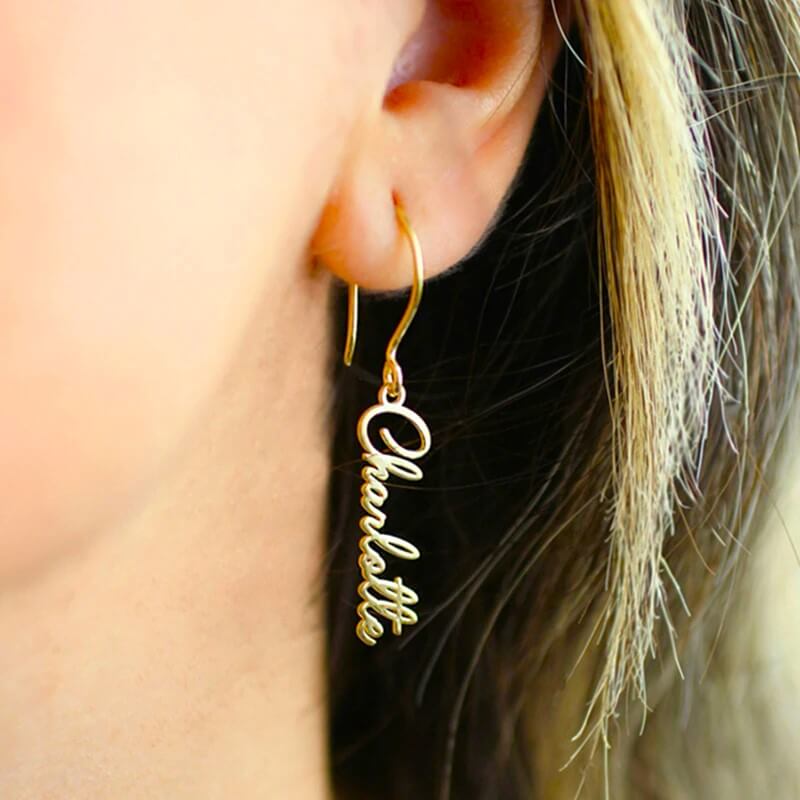 Woman wearing a gold nameplate dangle earrings with the name Chartolle